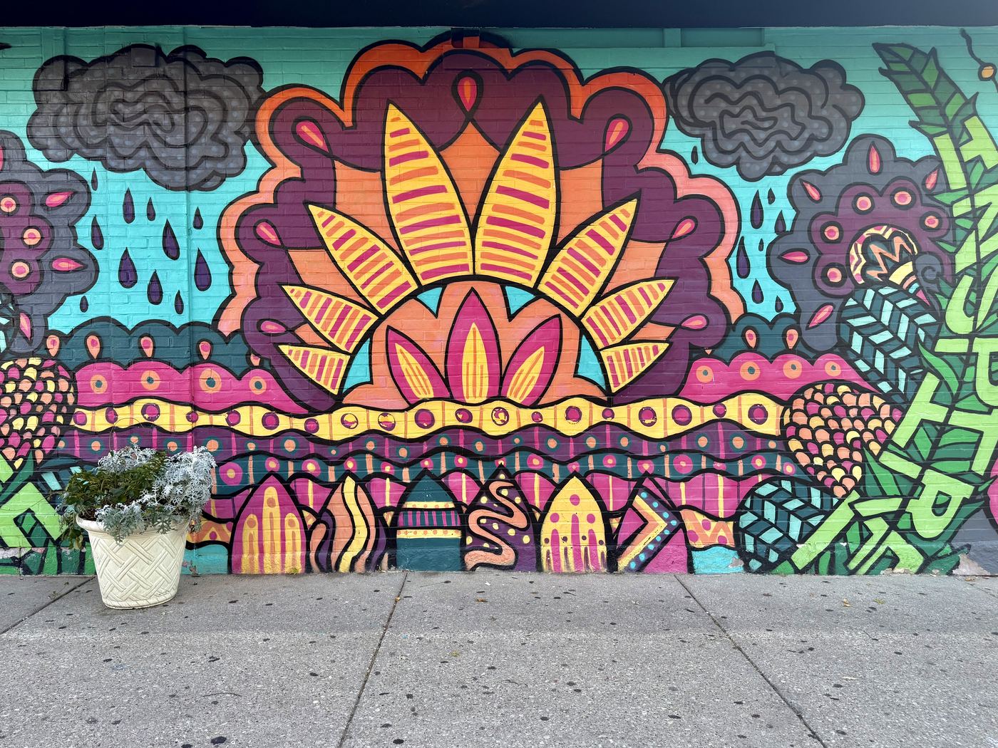 A colorful mural of a rising sun, flowers, and rain clouds painted on a brick wall in Rogers Park